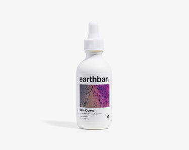 A bottle of 'earthbar Slim Down' herbal tonic with a dropper cap, predominantly white label with purple and pink speckles and text.