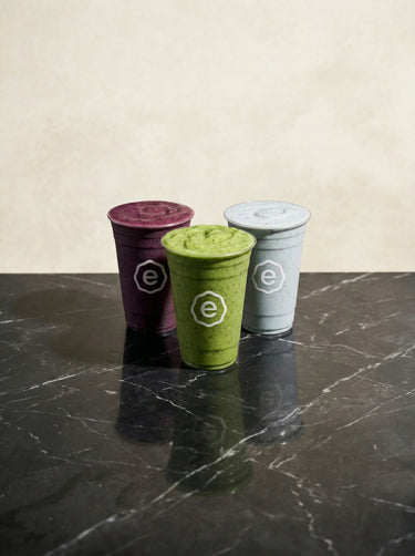 Three smoothie cups with different colored lids on a dark surface