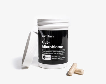 A jar of Earthbar's Gut+ Microbiome with 2 pills on the table next to it.
