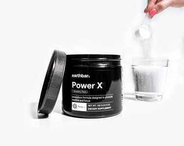 A woman pouring a scoop of Earthbar's Power X supplement into a glass of water.