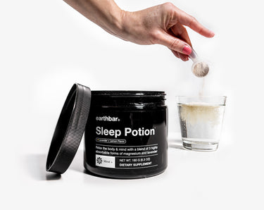 A woman taking a scoop of Earthbar's Sleep Potion and pouring it into a glass of water.