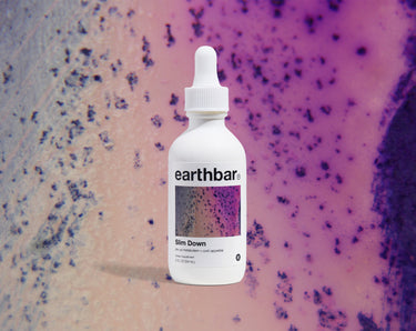 A bottle of 'earthbar Slim Down' herbal tonic with a dropper cap, predominantly white label with purple and pink speckles and text.