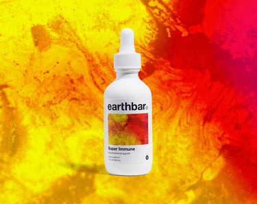 A bottle of 'Super Immune' herbal tonic by Earthbar with a dropper cap on an abstract yellow and red background