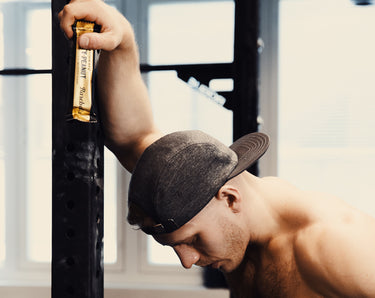 A man holding a Barebells protein bar in the gym.